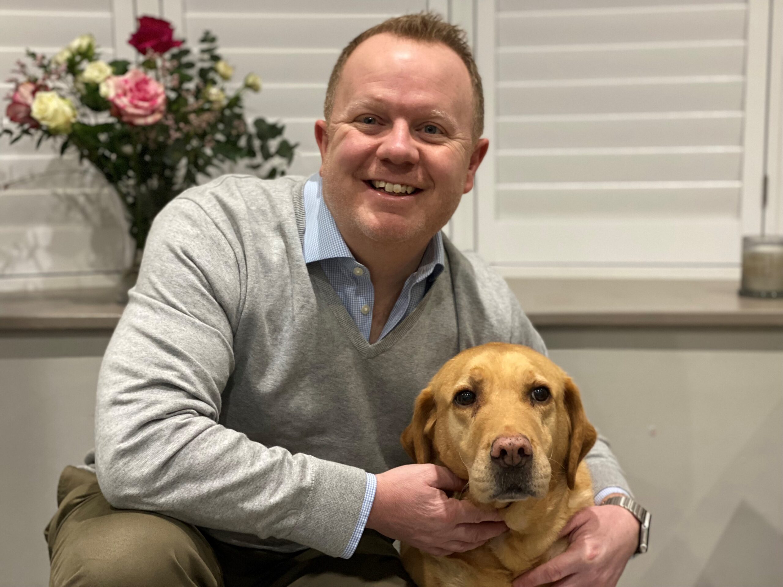 An imagine of Chris Shales, Clinial Director at Willows, sitting with a golden labrador and smiling