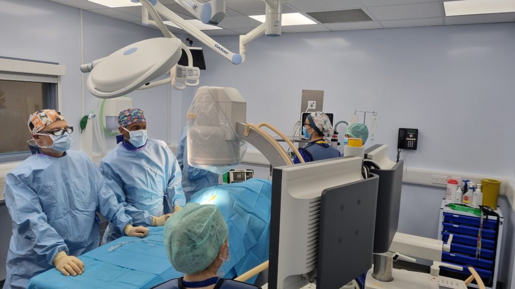 An image of the Cardiology team assembled in an operating theatre looking at a screen.