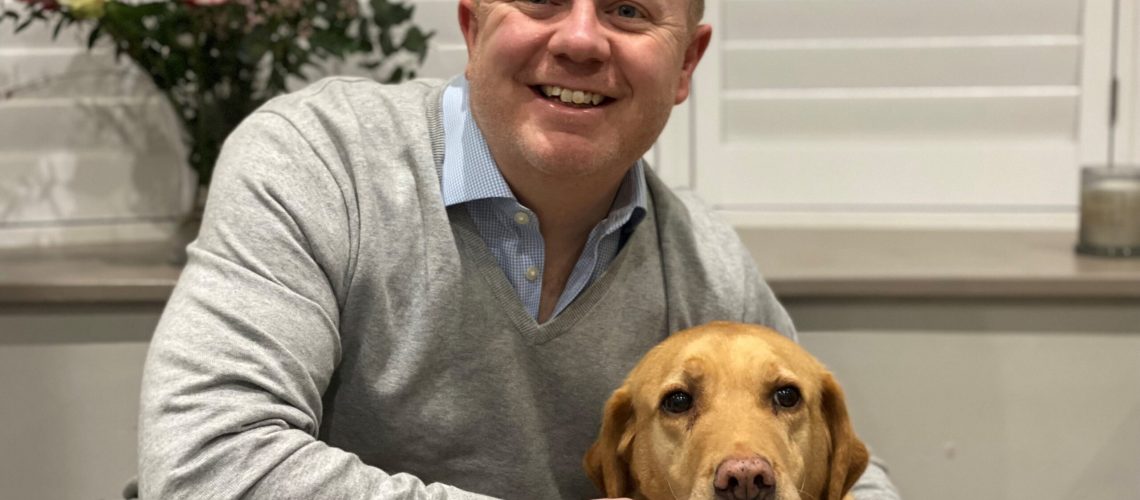 An imagine of Chris Shales, Clinial Director at Willows, sitting with a golden labrador and smiling